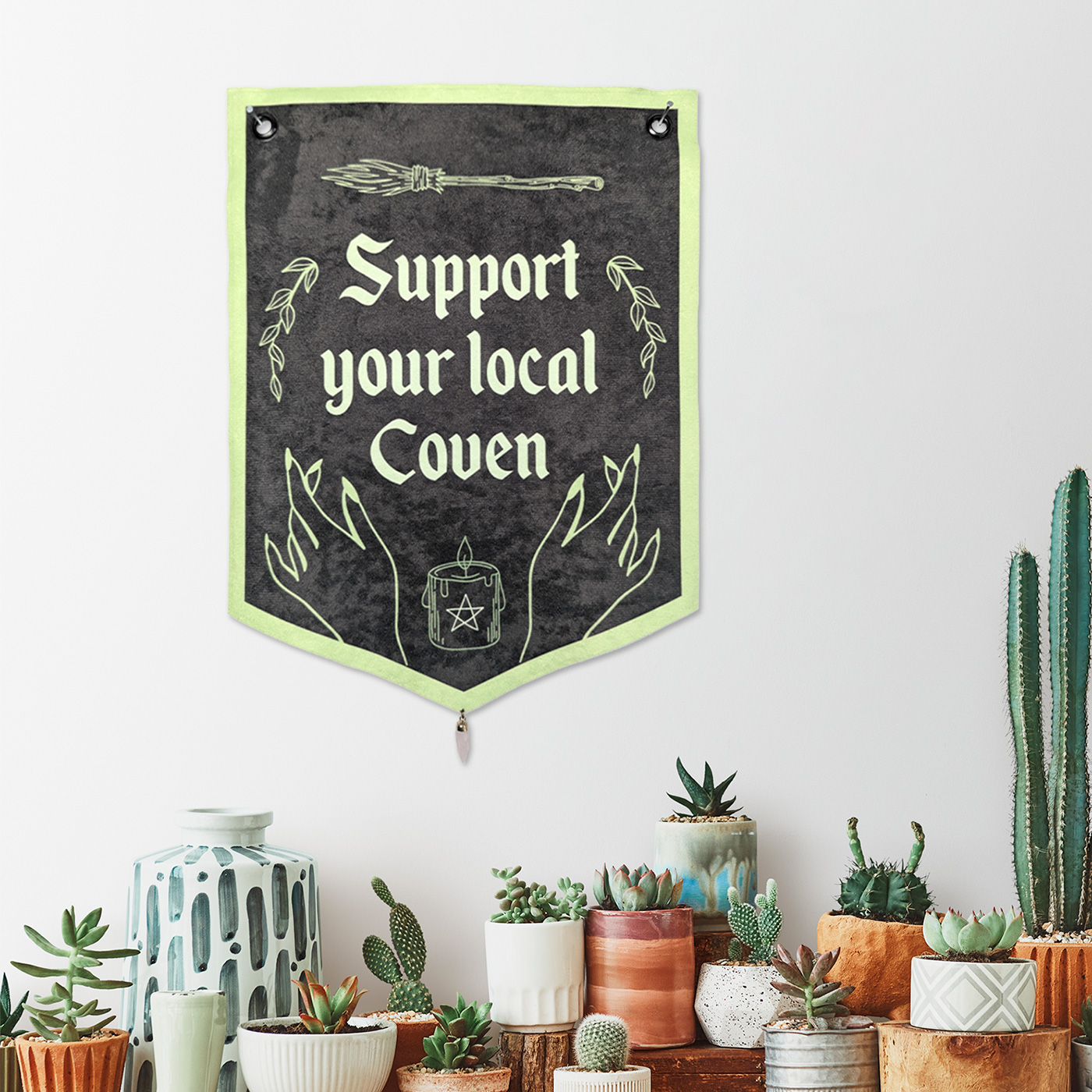 Decorative green fabric wall banner with stone pendant at the bottom. Text printed on the banner "Support your local coven"