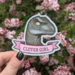 sticker with a raptor dinosaur and a pink banner with the text Clever Girl